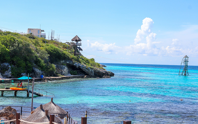 Panoramic image of Garrafon beach in Isla Mujeres showing hammocks and the sea in the background.