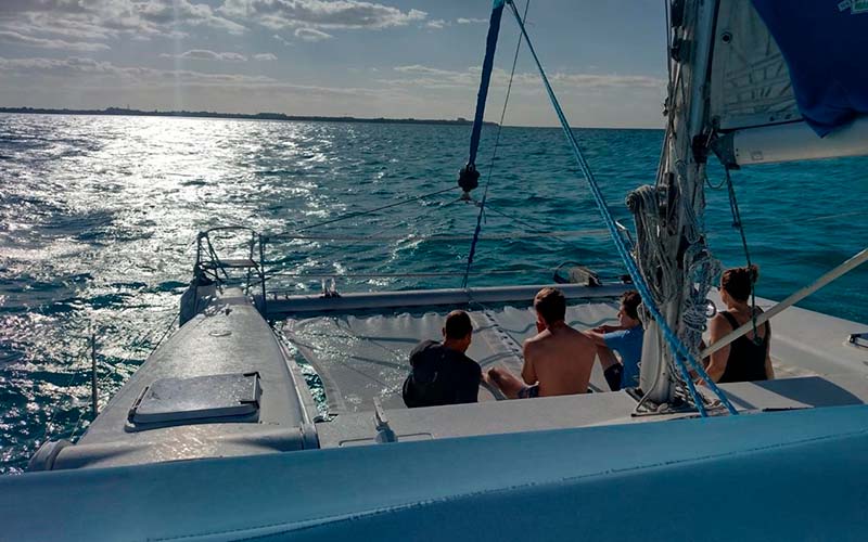 Group of people sitting on the catamaran looking at the horizon.